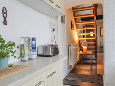 A kitchen counter with a toaster and stacked mugs next to a staircase with a small table and lamp at Awel Y Mor in Criccieth