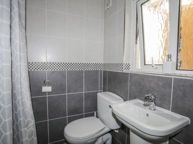 A bathroom with a toilet, sink, soap dispenser, shower curtain, and window at Awel Y Mor in Criccieth