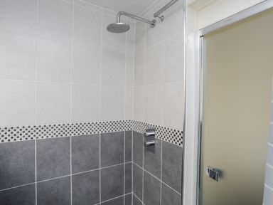 A shower area with grey and white tiles and a round shower head at Awel Y Mor in Criccieth