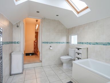 A bathroom with a bathtub toilet a laundry basket a window and a skylight at Awel Y Mor in Criccieth