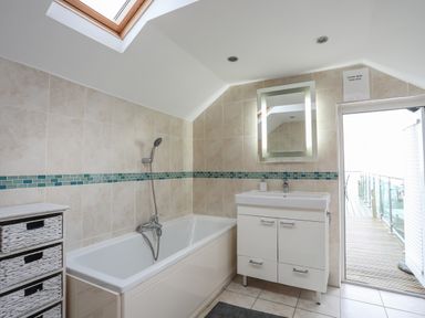 A bathroom with a bathtub a sink with cabinet and a door leading outside at Awel Y Mor in Criccieth