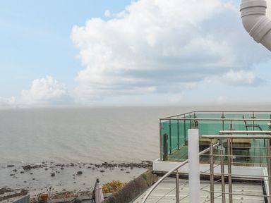 A balcony with glass railing and chairs overlooking a rocky shoreline and sea at Awel Y Mor in Criccieth