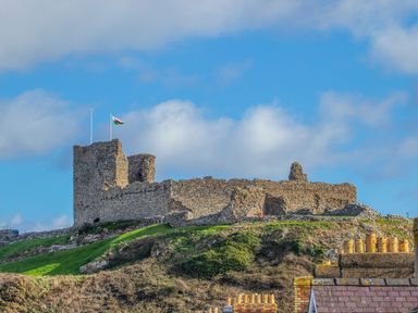 An old stone castle on a grassy hill with a flag flying at Awel Y Mor in Criccieth