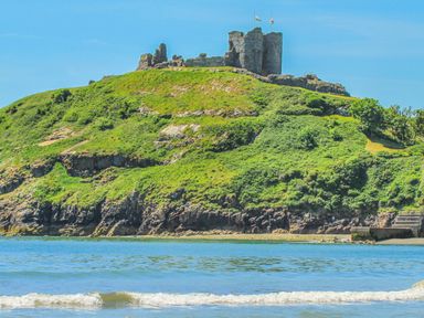 A hill with a stone castle ruin on top by the sea at Awel Y Mor in Criccieth