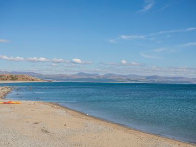 A sandy and pebbly beach with calm blue water and mountains in the distance at Awel Y Mor in Criccieth