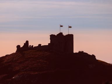 A silhouette of a castle with two flags on top against a sunset sky at Awel Y Mor in Criccieth