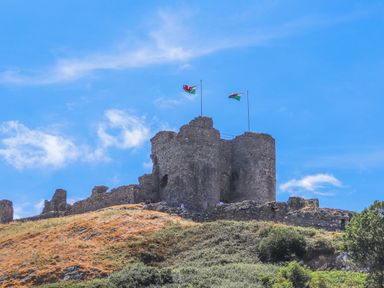 A stone castle ruin on a hill with two flags flying at Awel Y Mor in Criccieth