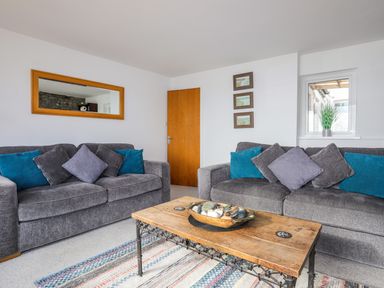 A living room with two gray sofas with blue and gray cushions a wooden coffee table with decorative items and a rug at Awel Y Mor in Criccieth