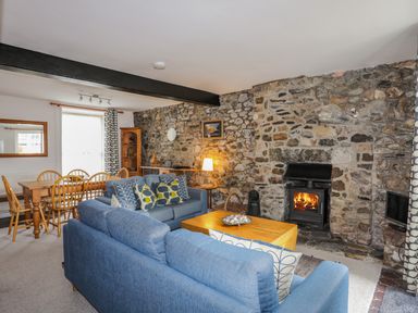 A living room with a stone fireplace blue sofas wooden dining table and chairs at Awel Y Mor in Criccieth