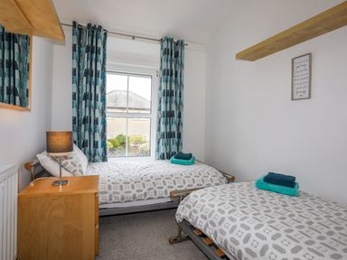 A bedroom with two single beds a window with blue patterned curtains and a bedside table at Awel Y Mor in Criccieth