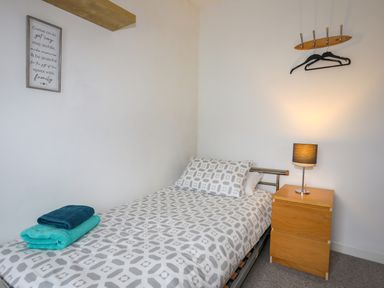 A bedroom with a single bed towel stack beside a wooden nightstand with lamp and a clothes rack on the wall at Awel Y Mor in Criccieth