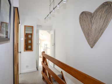 A hallway with wooden railing a wooden door mirror and a heart-shaped wall decoration at Awel Y Mor in Criccieth