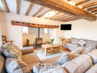 A living room with exposed wooden beams a wood stove two sofas a coffee table with flowers and a wall-mounted television at Plas Iolyn in Pentrefoelas near Betws-Y-Coed