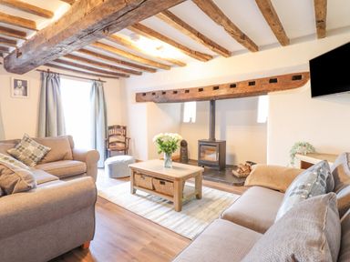A living room with wooden ceiling beams sofas a coffee table with flowers and a wood-burning stove at Plas Iolyn in Pentrefoelas near Betws-Y-Coed