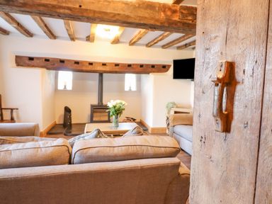 A living room with a wood stove a wooden beam ceiling and a sofa with flowers on a table at Plas Iolyn in Pentrefoelas near Betws-Y-Coed