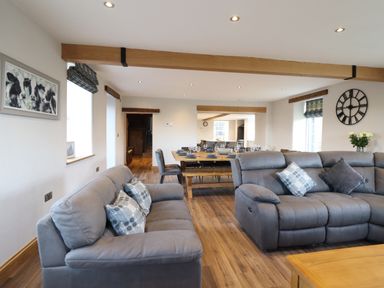 A living room with gray sofas and a dining table with chairs set for a meal at Plas Iolyn in Pentrefoelas near Betws-Y-Coed
