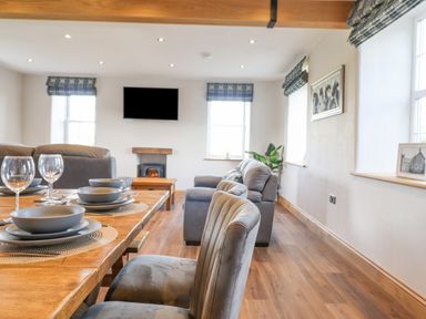A dining table set with bowls and glasses in a living room with sofas a wall-mounted television and a fireplace at Plas Iolyn in Pentrefoelas near Betws-Y-Coed
