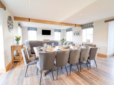 A dining room with a large wooden table set with dishes and glasses and gray chairs at Plas Iolyn in Pentrefoelas near Betws-Y-Coed