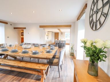 A dining area with a wooden table set with plates and glasses next to a kitchen area at Plas Iolyn in Pentrefoelas near Betws-Y-Coed