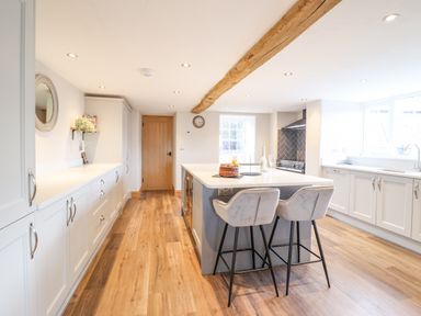 A kitchen with white cabinets an island with two bar stools wooden floor and a wooden door at Plas Iolyn in Pentrefoelas near Betws-Y-Coed