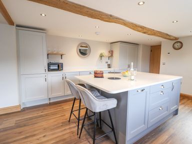 A kitchen with an island and bar stools and cabinets along the wall at Plas Iolyn Pentrefoelas near Betws-Y-Coed