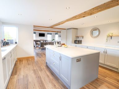 A kitchen with a large island and dining table visible through an open doorway at Plas Iolyn in Pentrefoelas near Betws-Y-Coed