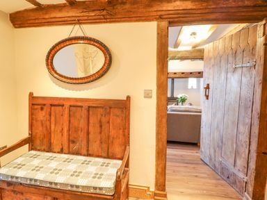 A wooden bench with a cushion below an oval mirror next to an open wooden door leading to a living room at Plas Iolyn in Pentrefoelas near Betws-Y-Coed