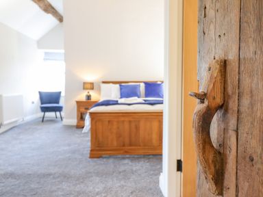 A bedroom with a wooden bed blue cushions a nightstand with a lamp and a blue chair at Plas Iolyn Pentrefoelas near Betws-Y-Coed