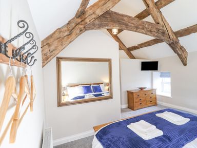 A bedroom with wooden beams a large mirror a wooden dresser a mounted television and a bed with blue bedding and folded towels at Plas Iolyn Pentrefoelas near Betws-Y-Coed