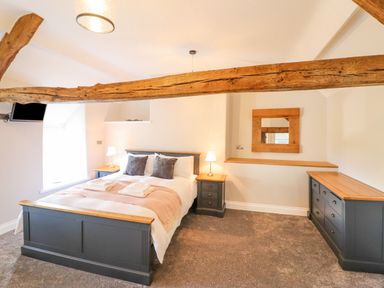 A bedroom with a double bed two bedside tables with lamps a chest of drawers a wooden beam across the ceiling and a wall mirror at Plas Iolyn in Pentrefoelas near Betws-Y-Coed