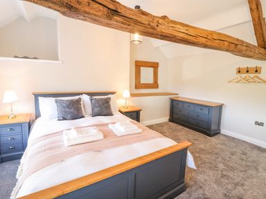 A bedroom with a double bed two bedside tables lamps a dresser and a mirror under exposed wooden beams at Plas Iolyn in Pentrefoelas near Betws-Y-Coed