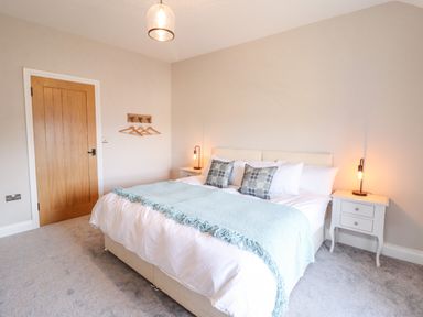 A bedroom with a bed with pillows and a blanket two bedside tables with lamps and a wooden door with hangers on the wall at Plas Iolyn in Pentrefoelas near Betws-Y-Coed