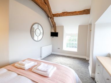 A bedroom with a bed, a round mirror on the wall, a TV mounted near a wooden beam, a window, and a chest of drawers at Plas Iolyn in Pentrefoelas near Betws-Y-Coed
