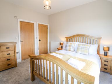 A bedroom with a wooden bed frame a dresser two bedside tables with lamps and two wooden doors at Plas Iolyn in Pentrefoelas near Betws-Y-Coed