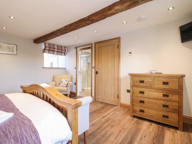 A bedroom with a wooden bed frame a chair a wooden dresser and an open door to a bathroom at Plas Iolyn in Pentrefoelas near Betws-Y-Coed