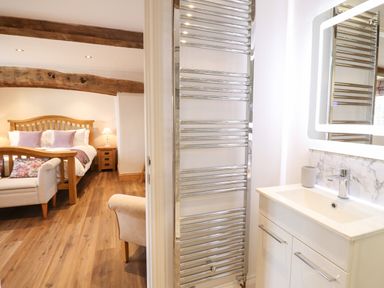 A bedroom with wooden bed and side table and a white sink with mirror in adjacent bathroom at Plas Iolyn in Pentrefoelas near Betws-Y-Coed