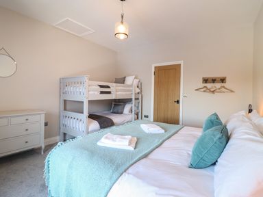 A bedroom with a double bed, bunk beds, a chest of drawers, a door, and wall hooks with hangers at Plas Iolyn in Pentrefoelas near Betws-Y-Coed
