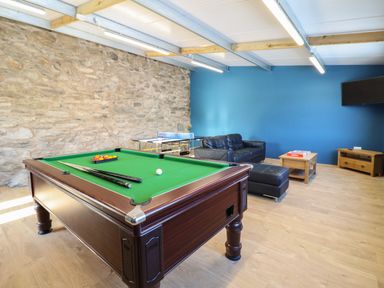 A game room with a pool table two cues a ping pong table a black leather sofa a wooden coffee table with a board game and a wooden TV stand at Plas Iolyn in Pentrefoelas near Betws-Y-Coed