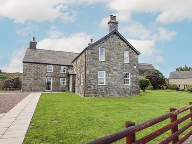 A stone house with white framed windows on green lawn near wooden fence at Plas Iolyn in Pentrefoelas near Betws-Y-Coed