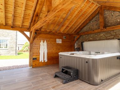 An outdoor covered area with a hot tub two white robes hanging on a wooden wall and steps to the hot tub at Plas Iolyn in Pentrefoelas near Betws-Y-Coed