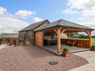 An outdoor area with a wooden pergola covering a hot tub bench and table next to a stone building at Plas Iolyn in Pentrefoelas near Betws-Y-Coed