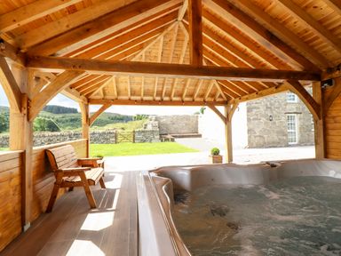 An outdoor wooden gazebo with a hot tub and a wooden bench overlooking a garden and stone wall at Plas Iolyn in Pentrefoelas near Betws-Y-Coed