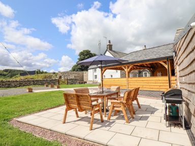 An outdoor patio area with wooden table and chairs under an umbrella and a barbecue grill at Plas Iolyn in Pentrefoelas near Betws-Y-Coed