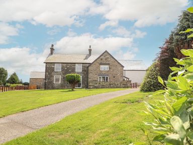 A stone house with two chimneys and a driveway surrounded by grass and trees at Plas Iolyn in Pentrefoelas near Betws-Y-Coed