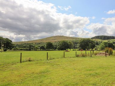 A grassy field with a wire fence and trees with hills in the background at Plas Iolyn in Pentrefoelas near Betws-Y-Coed