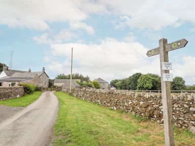A rural path between stone walls leading to stone houses with a wooden signpost showing directions at Plas Iolyn in Pentrefoelas near Betws-Y-Coed