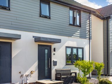 The exterior of a modern house with black doors, windows, a bench, and small bushes outside Sea View in Llanfaelog