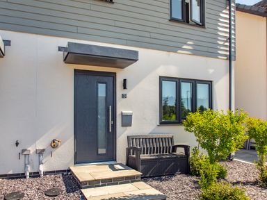The exterior entrance of a modern house with a dark door bench and small bushes at Sea View in Llanfaelog