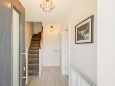 A hallway with carpeted stairs a closed white door light fixtures and wall art at Sea View in Llanfaelog