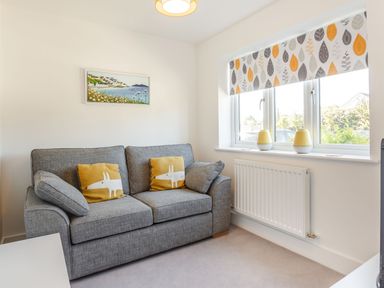 A small living room with a gray sofa with yellow cushions by a window with patterned blinds at Sea View in Llanfaelog